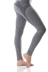 Close up side view of woman legs stretching the muscles of the foot in gray sports thermo-underwear with pattern on white background.