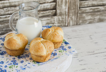 Homemade sweet brioche rolls and a pitcher of milk on a light rustic wood background