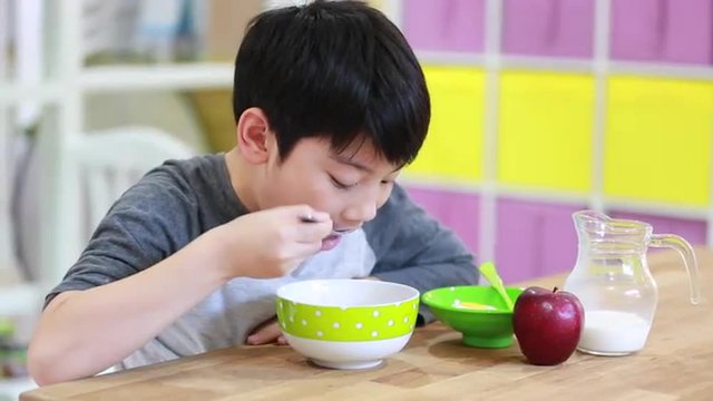 Little asian Boy eating cereal with milk with smile face