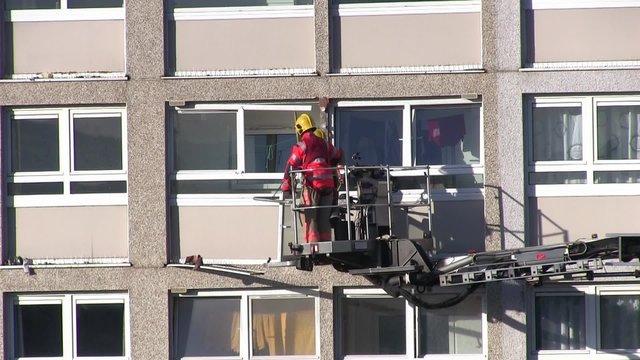Two fire fighters on a hydraulic platform clearing debris from a domestic apartment balcony following and accidental explosion of an aerosol can blew the front of the balcony out  