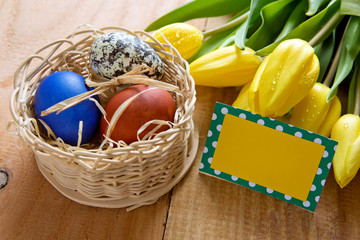 Easter basket with colored eggs and yellow tulips.