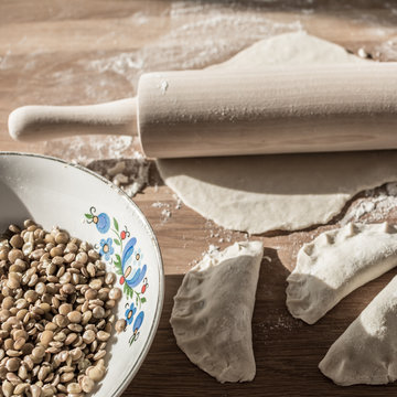 Traditional polish dumplings  - lentil filling in folk bowl, rolling pin and dough on breadboard. Square. 