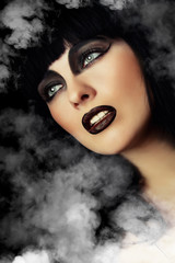 Portrait of a beautiful woman with dark make-up in a smoke