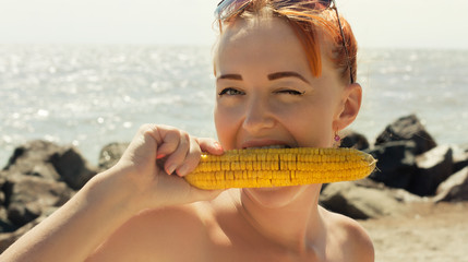 Funny woman eating boiled corn on the beach