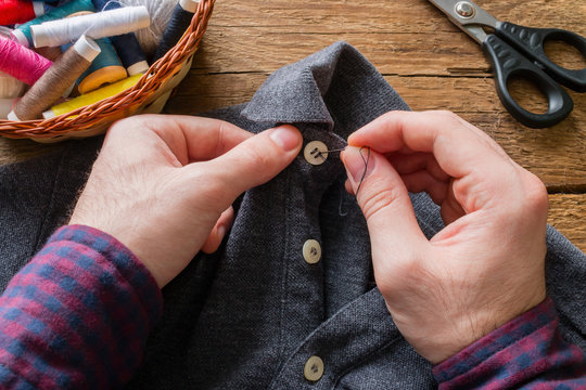 man sews a button to his shirt