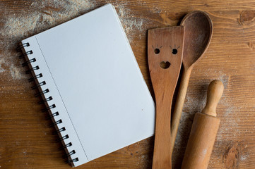 Open recipe book with wooden spoon, rolling pan and spatula