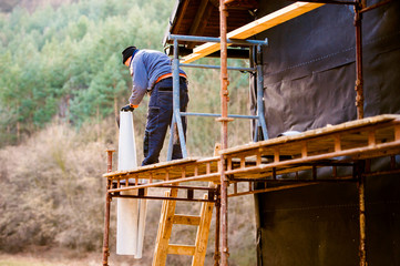 Construction worker on scaffold thermally insulating house, blac
