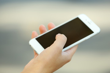 A female hand holding a mobile phone outdoors, on blurred background