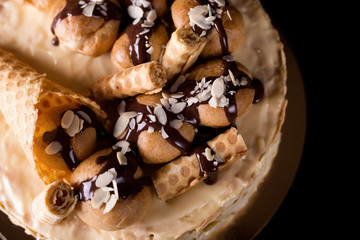 Napoleon cake on a dark wooden background decorated with petals of almonds eclairs, waffles and chocolate icing