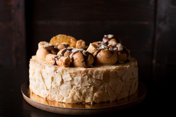 Napoleon cake on a dark wooden background decorated with petals of almonds eclairs, waffles and chocolate icing