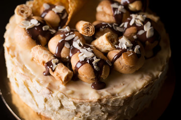 Napoleon cake on a dark wooden background decorated with petals of almonds eclairs, waffles and chocolate icing