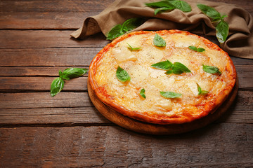 Tasty pizza decorated with basil and cotton napkin on wooden background