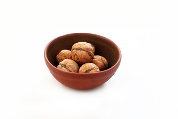 Целые грецкие орехи в коричневой керамической чашке на белом фоне