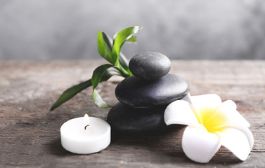 Fototapeta na wymiar Spa stones with candle, bamboo and tropical flower on wooden table against grey background