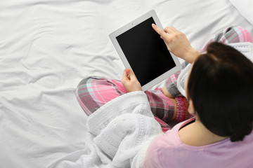 Woman in pajamas using a tablet on her bed
