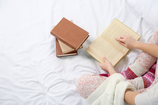 Woman in pajamas reading a book on her bed