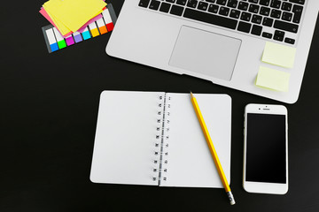 Workplace with mobile phone, laptop and stationery on black table