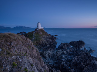 Llanddwyn Lighthouse Newborough, Anglesey, Cymru, North Wales in last light and a calm sea, with rocks in the foreground.