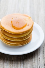 Stack of homemade pancakes with honey on wooden background.