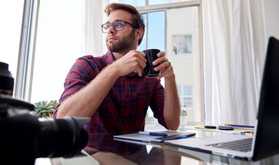 Young photographer holding coffee at his home studio