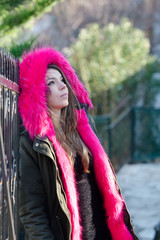 Pretty lady outside in cold weather, wear jacket with red hood leaning on handrails