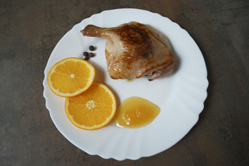 Cooked duck leg with orange and honey on white dish.