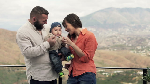 Young, happy family standing with cute small baby on the terrace
