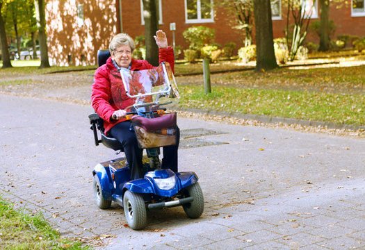 Seniorin mit Elektromobil  f&auml;hrt auf der Stra&szlig;e und winkt