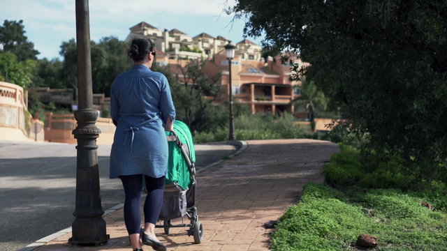 Young mother walking with perambulator in the small city
