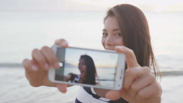 Selfie woman taking photos using smartphone having fun outside on beach. Smart phone screen showing as girl takes self portrait photo pictures outdoors at beach sunset. RED EPIC SLOW MOTION.