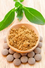 Herbal powder in wooden spoon on herb tablet.