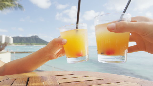 Beach bar party drinking friends toasting Hawaiian sunset cocktails having fun. Close up of woman holding alcoholic drink cheering in Waikiki beach, Honolulu, Oahu, Hawaii, USA. RED EPIC SLOW MOTION.