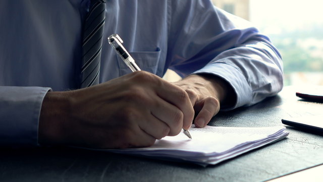 Businessman signing documents sitting by table in office
