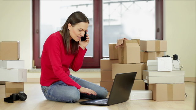 Shopping woman at home surfing the internet and talking on the phone besides stack of boxes