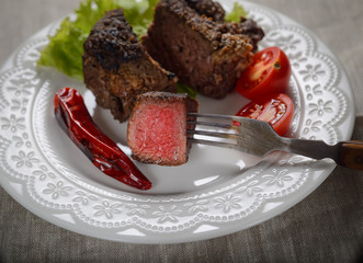 piece of steak on a fork, salad and vegetables