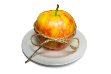 Apple tied with twine on a white plate closeup