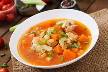 Tomato chicken soup with pumpkin, beans and celery in white bowl