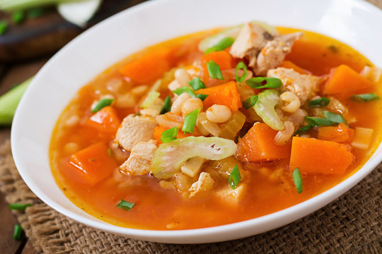 Tomato chicken soup with pumpkin, beans and celery in white bowl
