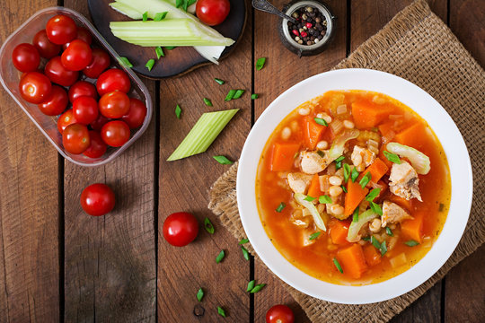 Tomato chicken soup with pumpkin, beans and celery in white bowl. Top view