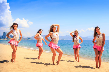 cheerleaders stand on beach hold hands on hip against azure sea