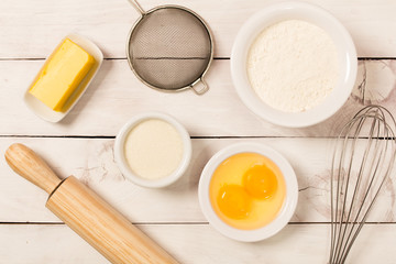 Baking in rustic kitchen recipe ingredients (eggs, flour, milk, butter) on white  wooden table from above. 