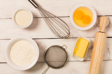 Baking in rustic kitchen recipe ingredients (eggs, milk, butter, sugar) on white  wooden table from above. 