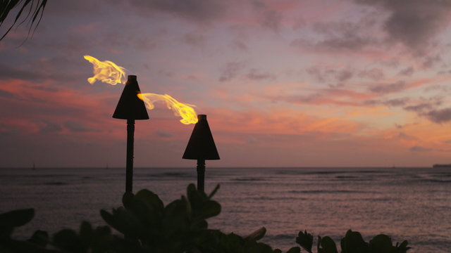 Torch fire flames burning on Waikiki Beach on Oahu, Hawaii at sunset sky by palm trees. Beautiful slow motion torches on Hawaiian beach. RED EPIC SLOW MOTION.