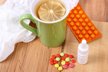 Pills and nose drops for colds, handkerchiefs and hot tea with lemon