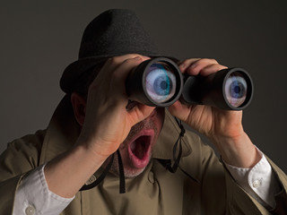 Fototapeta Photograph of a man in trench coat and hat looking through binoculars with huge, cartoonish eyes seen in the lenses. obraz