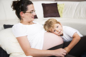 Pregnant woman is playing with her first child. Litte Child is listen to her stomach
