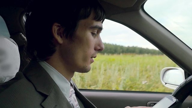Young handsome dark-haired man driving car in the field and speaking on mobile phone in slowmotion. HD. 1920x1080