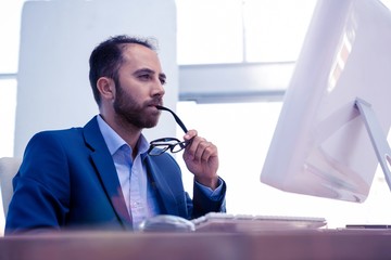 Businessman holding eyeglasses while looking at computer 