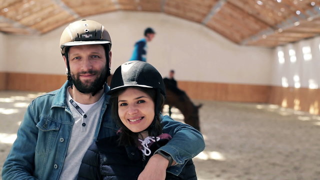 Portrait of happy couple with helmet on the riding lesson at the stable
