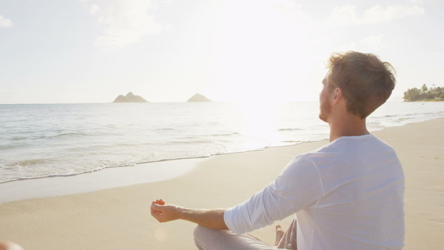 Meditation and Yoga. People meditating in lotus pose relaxing outside on beach at sunrise. Couple woman and man in serene ocean landscape. Lanikai beach, Oahu, Hawaii, USA.